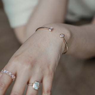 Lab diamond toi et moi bangle in yellow gold worn on the wrist, styled with an emerald cut ring on the hand.