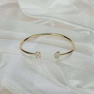 Lab grown diamond toi et moi bangle in yellow gold on satin fabric, emerald cut and pear shape stones at the open ends.