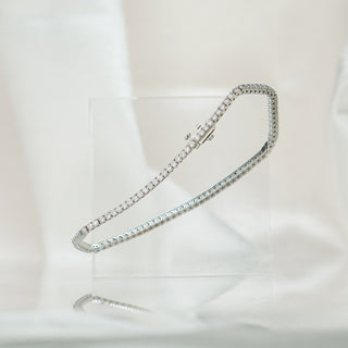 Lab grown diamond tennis bracelet in white gold draped over a clear acrylic block against soft fabric.