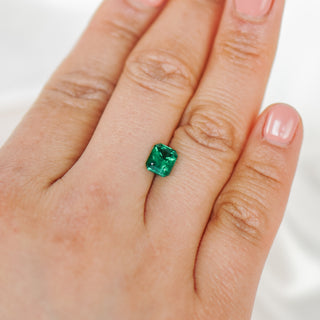 A close-up of a hand wearing a single cushion-cut green gemstone ring on the ring finger, set against a soft white background.