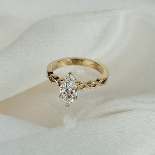 Marquise lab grown diamond solitaire engagement ring in yellow gold on satin fabric, braided shank beneath the prong set center.