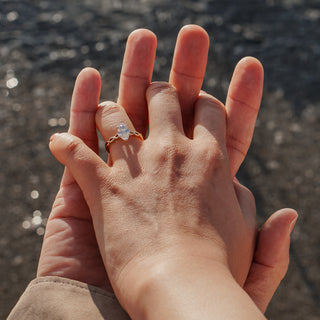 Marquise solitaire engagement ring worn on the hand holding a child's hand at the water, braided band catching sunlight.