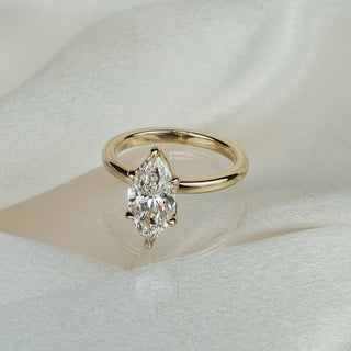 Marquise lab grown diamond flower head solitaire in yellow gold on satin fabric, sculptural prongs on a plain band.