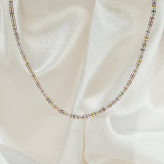 Natural multi-color Sapphire tire bead necklace on white satin fabric, pastel beads in a continuous strand.