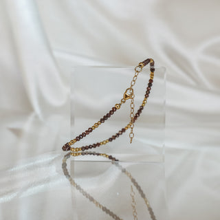 Grey gold-accented brown raw faceted Diamond bracelet draped over a clear acrylic block, clasp and extension chain visible.