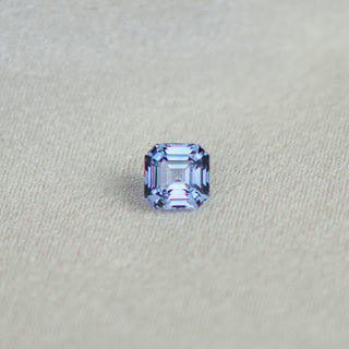 An emerald-cut light blue sapphire, displayed on a textured light beige fabric background.