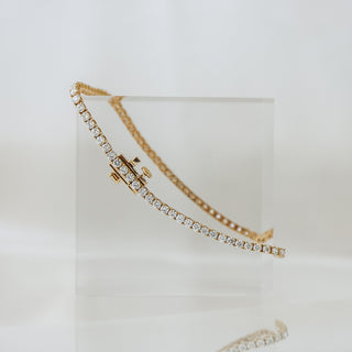 Natural Diamond tennis bracelet in yellow gold resting on an acrylic block, continuous line of prong set stones.