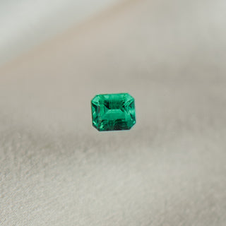 A single emerald-cut green emerald centered on a soft, textured beige fabric background.