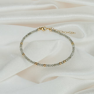 Natural grey raw faceted Diamond bracelet on white satin fabric, 68 grey diamonds with yellow gold beads and clasp visible.