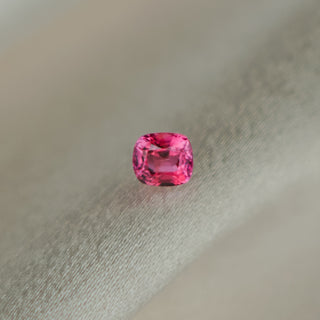 A cushion-cut pink sapphire, resting on a textured light gray fabric surface.