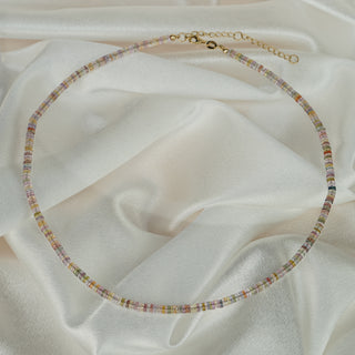Full circle view of a multi-color Sapphire tire bead necklace on satin, 18k yellow gold clasp and extender chain visible.
