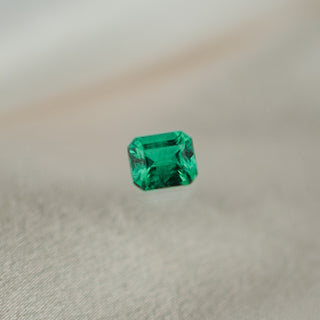 A single emerald-cut green gemstone, displayed on a soft, light beige textured fabric surface.