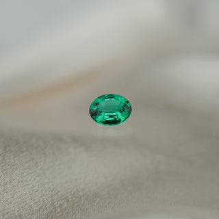 A single oval-cut emerald green gemstone centered on a soft, light beige fabric background.