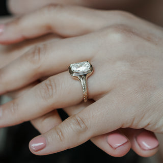 Lab grown diamond engagement ring with old mine cushion cut center worn on the hand, engraved shank visible in yellow gold.