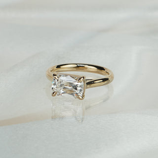 Old mine cut lab grown diamond engagement ring in yellow gold on satin fabric, center stone set east-west in claw prongs.