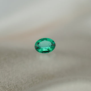 A single oval-cut green gemstone with a faceted cut, resting on a soft, light gray fabric surface.