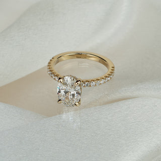 Oval lab grown diamond hidden halo engagement ring in yellow gold on satin fabric, pavé Diamonds running the shank.