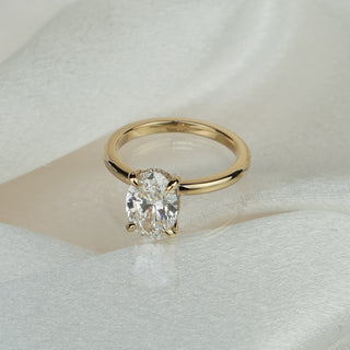 Oval lab grown diamond hidden halo solitaire in yellow gold on satin fabric, plain polished band beneath the four-prong center.