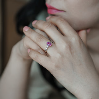 Close-up of a hand wearing a ring with a pink gemstone, blurred background
