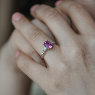 Pink Sapphire three-stone ring worn on the hand, oval center with pear shape Diamond sides in white gold.