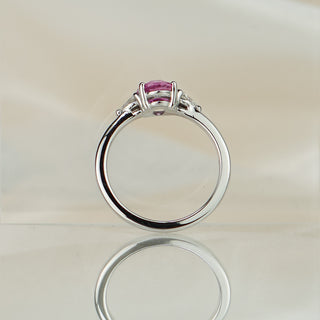 Oval pink Sapphire engagement ring standing upright with reflection, three stones across the top in white gold.