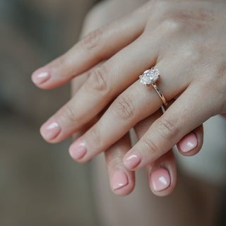 Oval hidden halo solitaire worn on the hand, clean yellow gold band with concealed round brilliants under the stone.