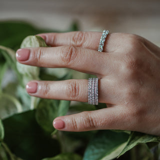 White gold micro pavé band worn stacked with other bands on the hand against green leaves.