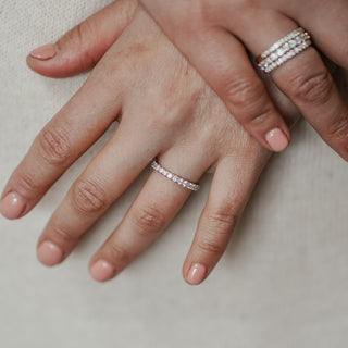 Close-up of two hands wearing diamond rings on a neutral background