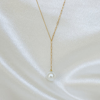 A delicate gold Y-necklace featuring a single white freshwater pearl pendant, displayed on a draped white satin fabric.