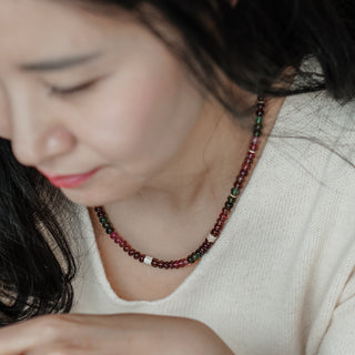 Multi-color Tourmaline bead necklace worn just below the collarbone, pink, green, and berry tones over a white knit top.