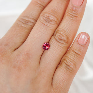 A close-up of a hand wearing a small round brilliant-cut pink gemstone ring on the ring finger.