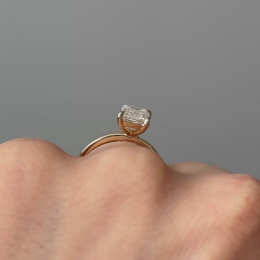 Video of a yellow gold emerald cut lab grown diamond pipe shank solitaire worn on the hand, step facets and rounded band in motion.