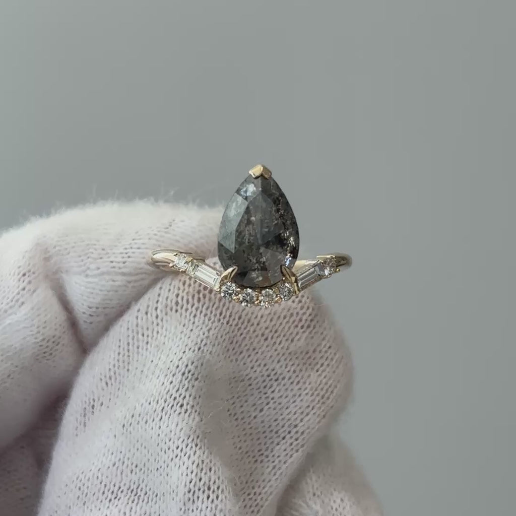 Video of a yellow gold salt and pepper rose cut pear engagement ring on a gloved hand, grey inclusions shifting through the light.