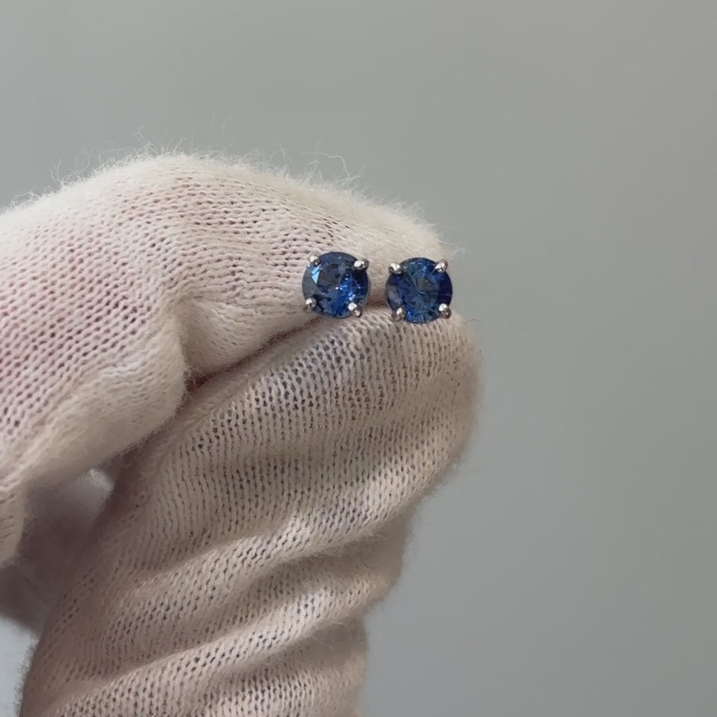 Video of natural blue Sapphire stud earrings held on a gloved hand, round brilliant stones showing depth of blue in motion.
