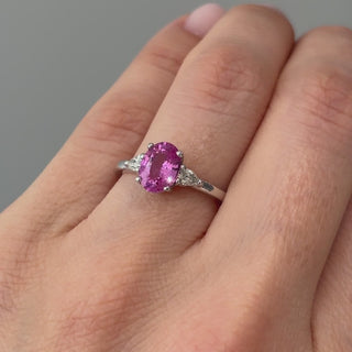 Video of a white gold oval pink Sapphire three-stone engagement ring worn on the hand, pink center in motion between the pear Diamonds.