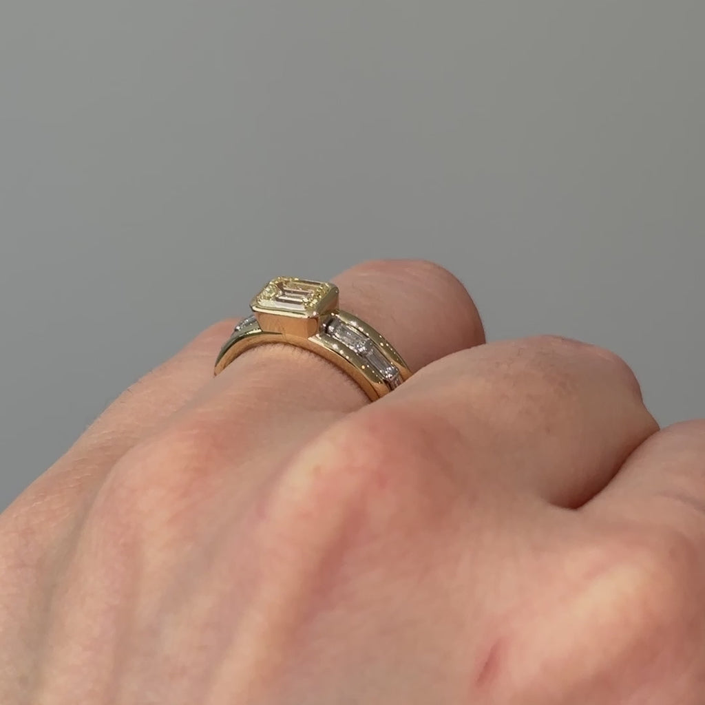Video of a two-tone natural yellow Diamond engagement ring worn on the hand, emerald cut center and mixed metals turning through the light.