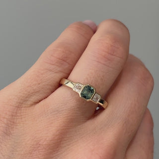 Video of a yellow gold teal Sapphire three-stone engagement ring worn on the hand, teal center moving between green and blue in the light.