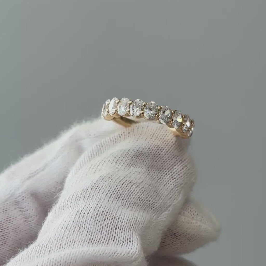 Video of a yellow gold lab grown diamond oval cut band on a gloved hand, oval stones turning through the light.