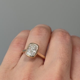 Video of a yellow gold cushion cut lab grown diamond bezel solitaire worn on the hand, enclosed stone turning through the light.