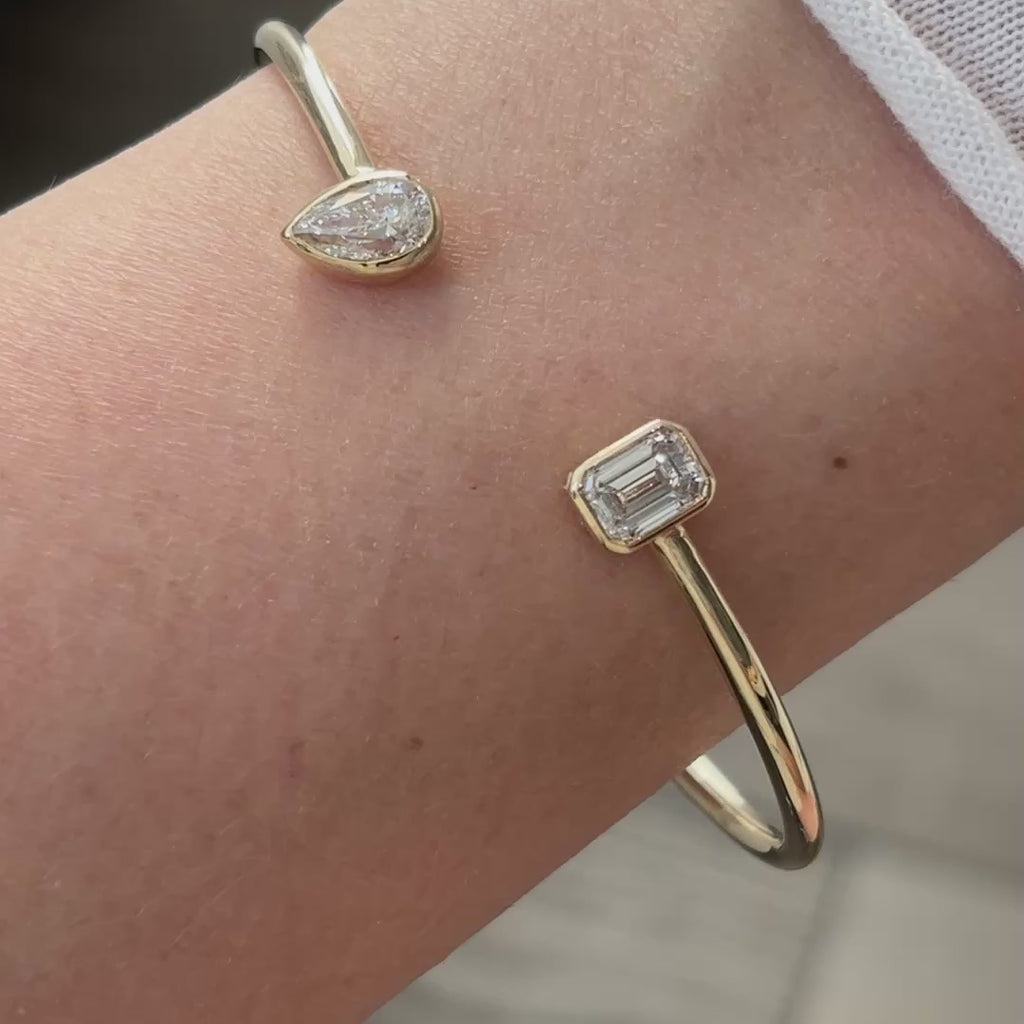 Video of a yellow gold lab grown diamond toi et moi bangle worn close on the wrist, emerald cut and pear stones in motion.