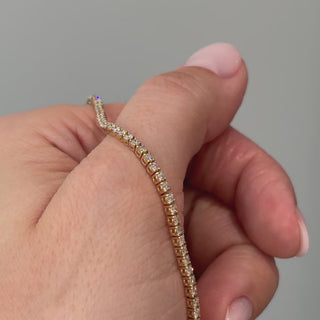 Video of a yellow gold lab grown diamond tennis bracelet held in hand, stones catching light along the full length.