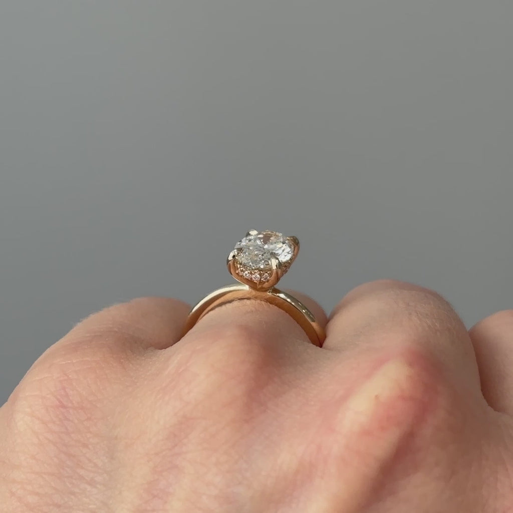 Video of a yellow gold oval lab grown diamond hidden halo solitaire worn on the hand, brilliance spreading from beneath the stone in motion.