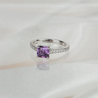 Asscher cut purple Sapphire engagement ring in white gold on satin fabric, cathedral setting with pavé Diamonds along the shank.