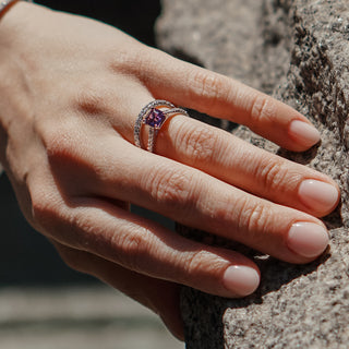 Purple Sapphire engagement ring worn on the hand outdoors, Asscher cut center in a cathedral setting.