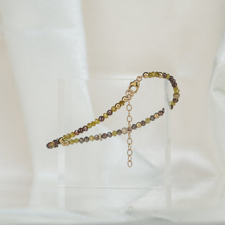 Natural yellow and brown Diamond bead bracelet draped over a clear acrylic block, extension chain hanging in frame.

