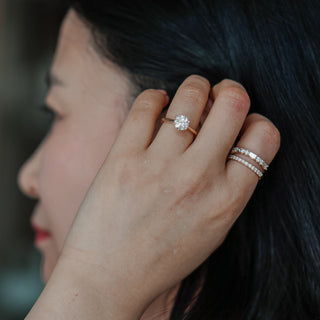 Close-up of a woman's hand with a diamond ring and two additional bands, putting hair behind ears.