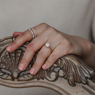 Round flower head solitaire worn on the hand resting on carved woodwork, elevated center in yellow gold.