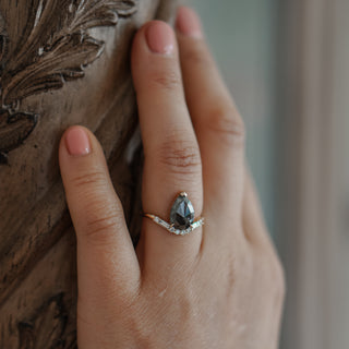 Natural salt and pepper Diamond ring worn on the hand against carved woodwork, pear center over accent stones.