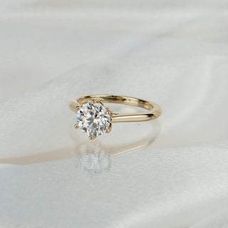 Round brilliant lab grown diamond flower head solitaire in yellow gold on satin fabric, six prongs on a cathedral shank.