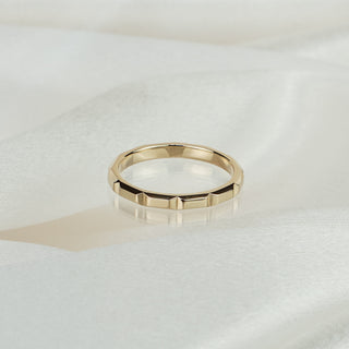 14k yellow gold faceted wedding band on white satin fabric, geometric flat panels cut around the exterior.